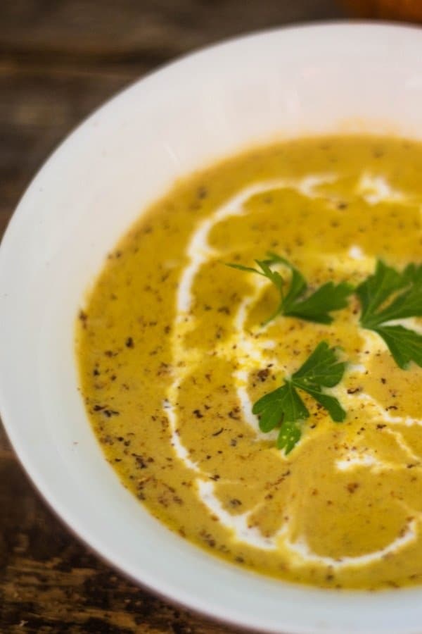 Harvest Pumpkin Soup in a white soup bowl topped with creme fraiche, parsley, and freshly grated nutmeg.