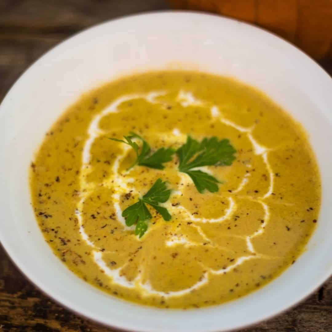 A pumpkin soup recipe that is full of flavors and a total comfort soup in a white soup bowl with black pepper, fresh nutmeg, and creme fraiche