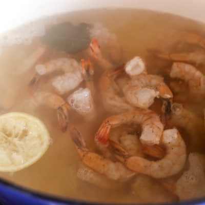 Fresh shrimp in poaching liquid in a large Dutch oven to make amazing poached shrimp.