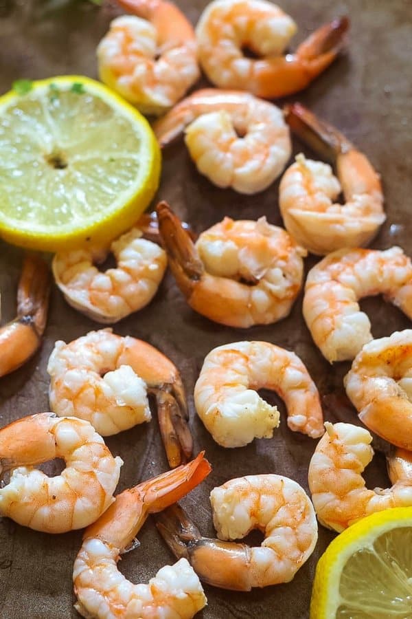 Fresh poached shrimp on a large platter with lemon slices scattered over the platter.