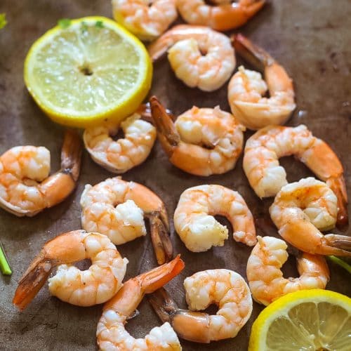 the easiest poached shrimp on a large brown platter with lemon wedges