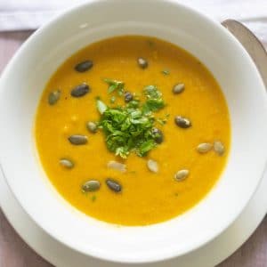 Hearty carrot coconut soup in a white soup bowl topped with pepitas and chopped herbs