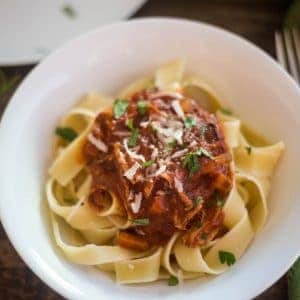 Hearty Pork ragu over pappardelle pasta sprinkled with fresh parsley and fresh grated parmesan reggiano in a white pasta bowl.