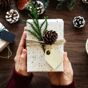 A gift wrapped with pretty white paper,a ribbon, green pine,and a pinecone.