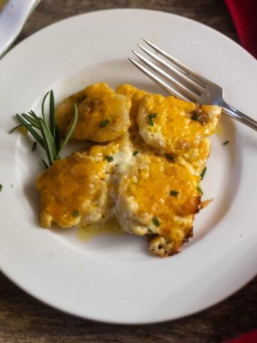 Easy Cheesy Scalloped Potatoes garnished with fresh rosemary on a white plate