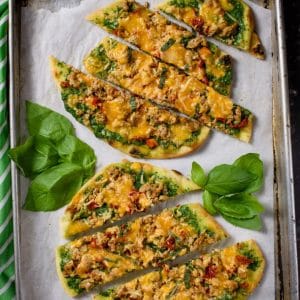 Cheesy Spinach Arugula Pesto Pizza sliced on parchment paper on a baking sheet with basil leaves sprinkled on the tray.