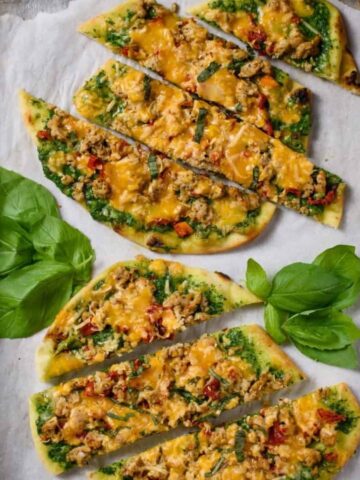 Cheesy Spinach Arugula Pesto Pizza sliced on parchment paper on a baking sheet with basil leaves sprinkled on the tray.