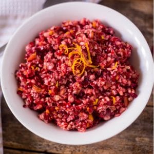 Flavorful fresh cranberries and oranges made into a delicious cranberry orange relish in a white serving bowl topped with orange zest.