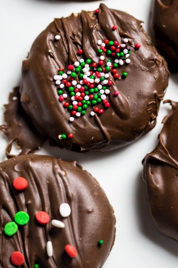 Peppermint patties one a white plate, one peppermint has green white and red sprinkle dots and the other peppermint patty has flat sprinkles.