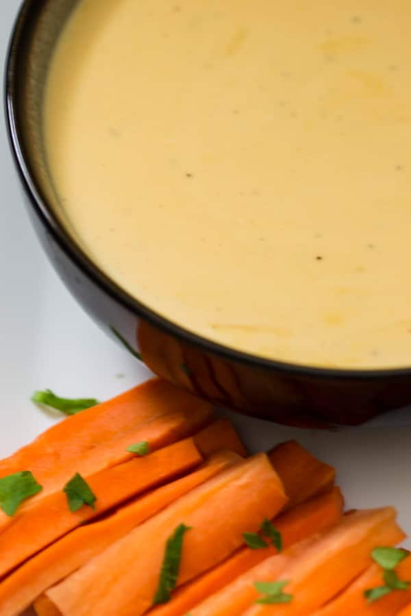 Savory beer cheese dip in a bowl with fresh cut carrots to the side to be dipped into the cheese dip.