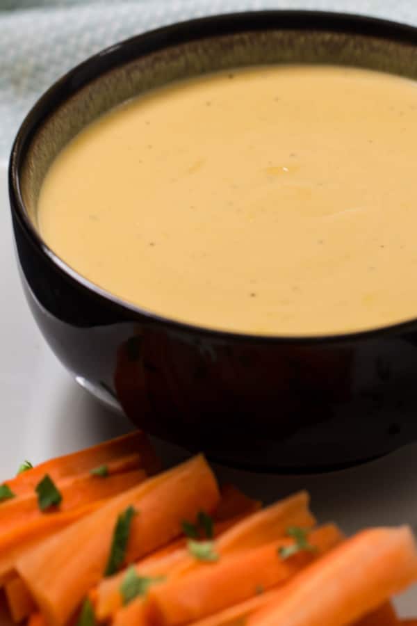Beer cheese dip in a brown bowl with carrot sticks sprinkled with parsley on the side.