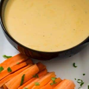 Tasty beer cheese dip with fresh carrots on a side white platter.