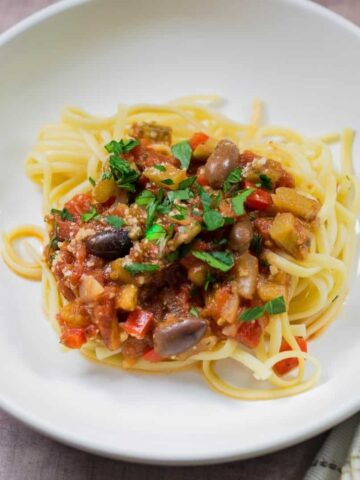 Eggplant pasta served in a white pasta bowl, sprinkled with parsley