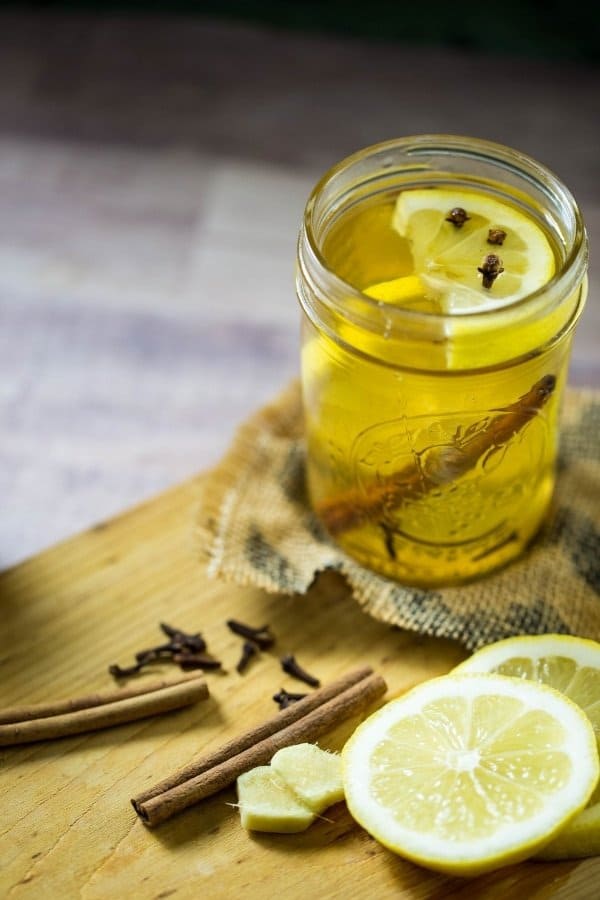 A warm hot toddy in a mason jar garnished with cinnamon stick, lemon wedge and cloves on a wooden board.