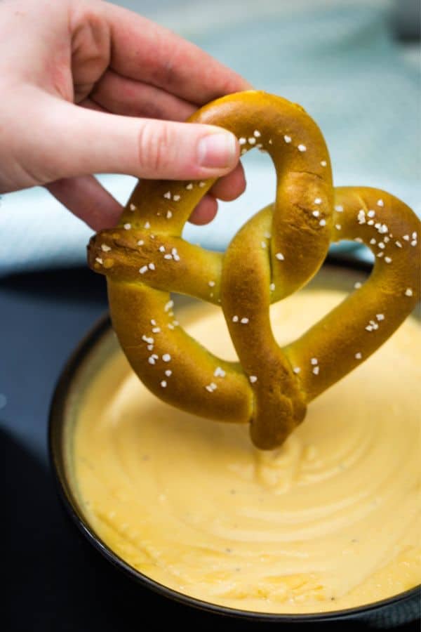 A Homemade pretzel being dipped into hot beer cheese dip for a great snack.