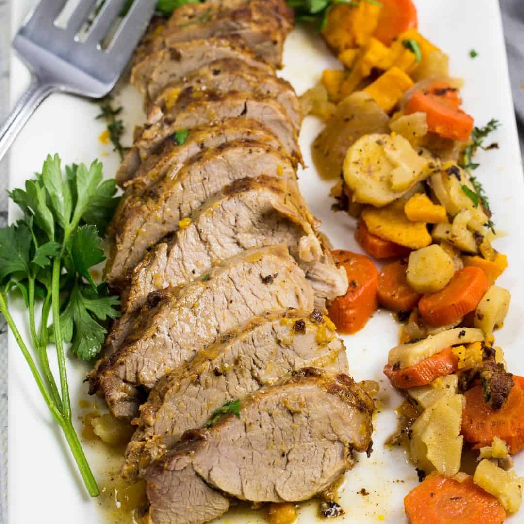 Sliced pork tenderloin with root veggies on a white platter