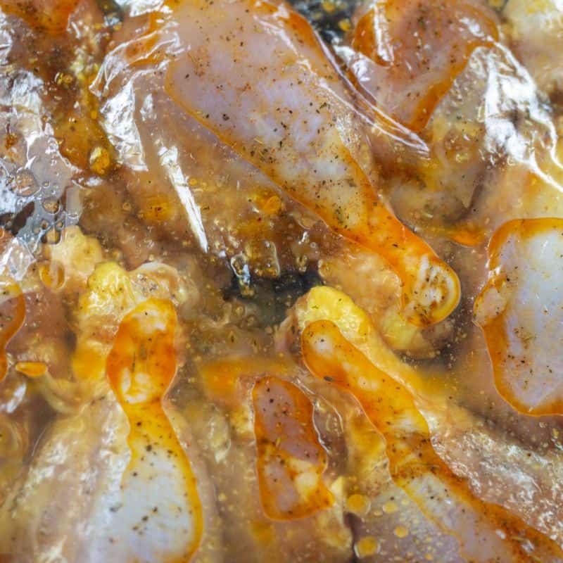 Chicken drumsticks marinating in a large plastic storage bag to be baked after marinating.