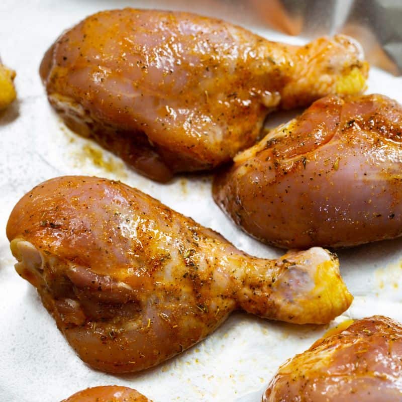 Marinated chicken legs on a baking sheet ready to be baked in the oven.