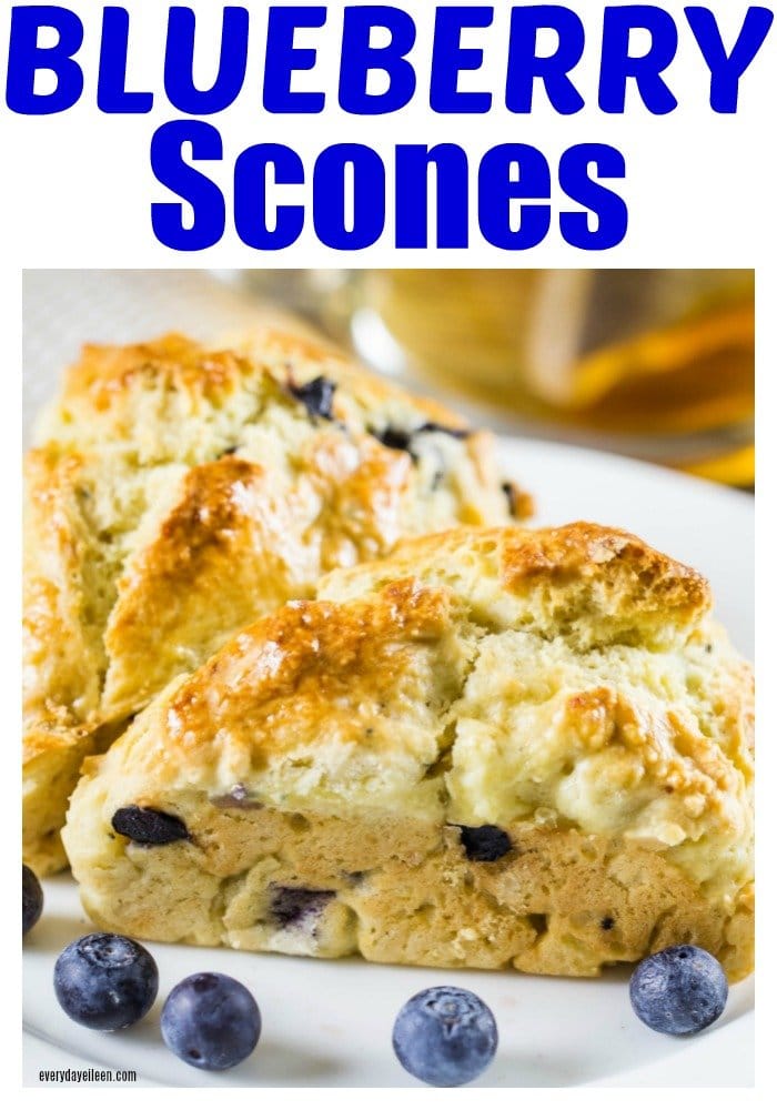 Delicious blueberry scones on a plate with fresh blueberries scattered around the scone.