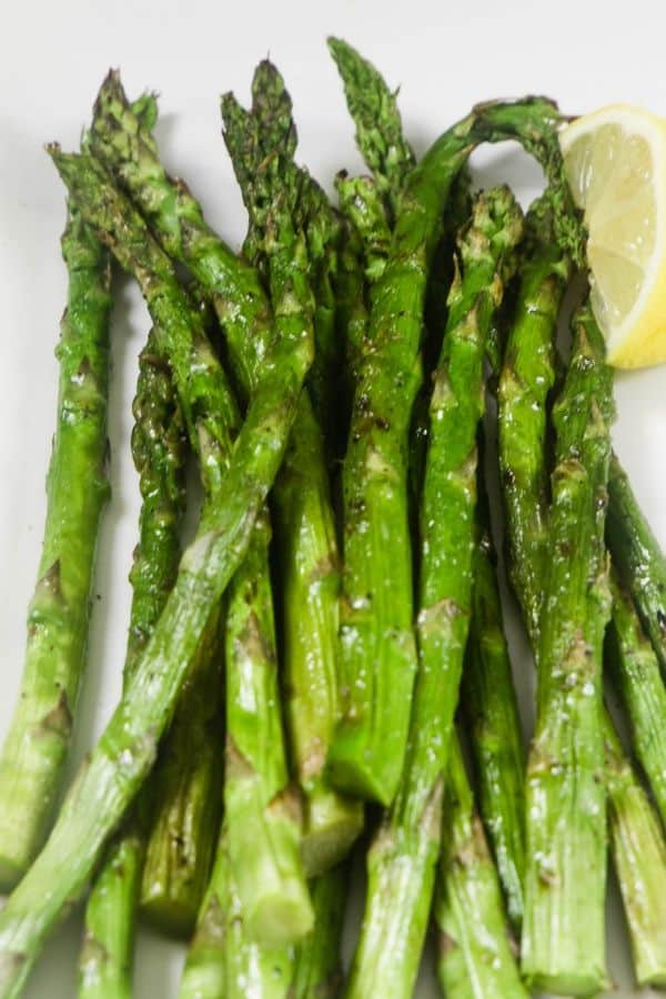 Grilled asparagus with a lemon wedge on a white platter