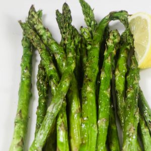 Tender asparagus on a white plate that has been grilled with a lemon wedge on the side