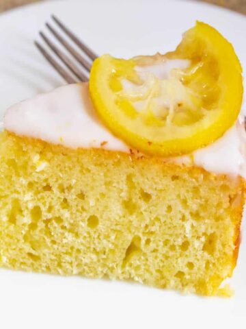Light and moist yogurt cake with a lemon wedge on a white plate.