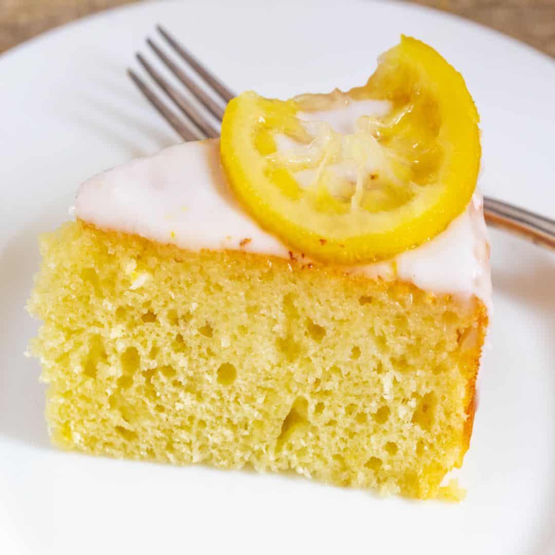 Light and moist yogurt cake with a lemon wedge on a white plate.