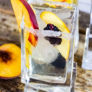 Peach sangria in a square glass filled with ice and peach slices and a sugar rim on the glass.