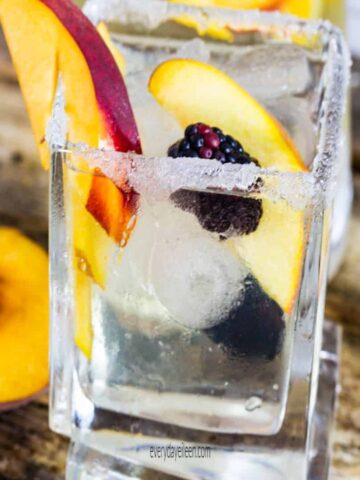 Peach sangria in a square glass filled with ice and peach slices and a sugar rim on the glass.