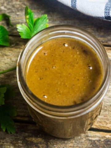 Homemade enchilada sauce in a mason jar with fresh herbs and a linen around the jar.