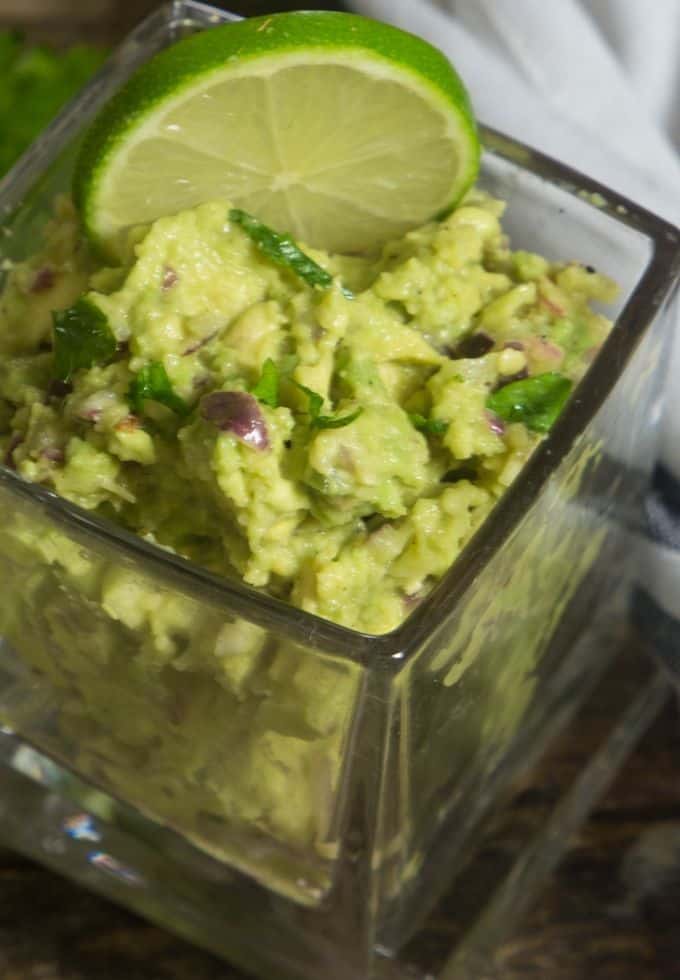 Easy homemade guacamole in a glass jar with a fresh lime wedge in the guacamole.