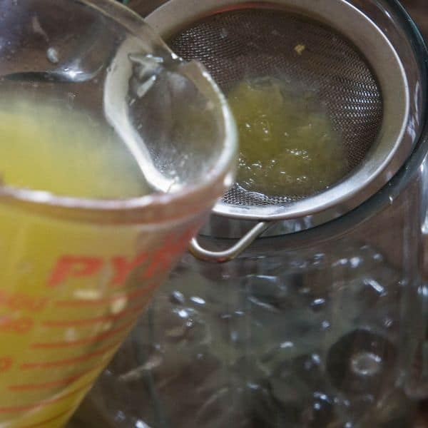 lemon juice being poured into a pitcher to make lavender lemonade