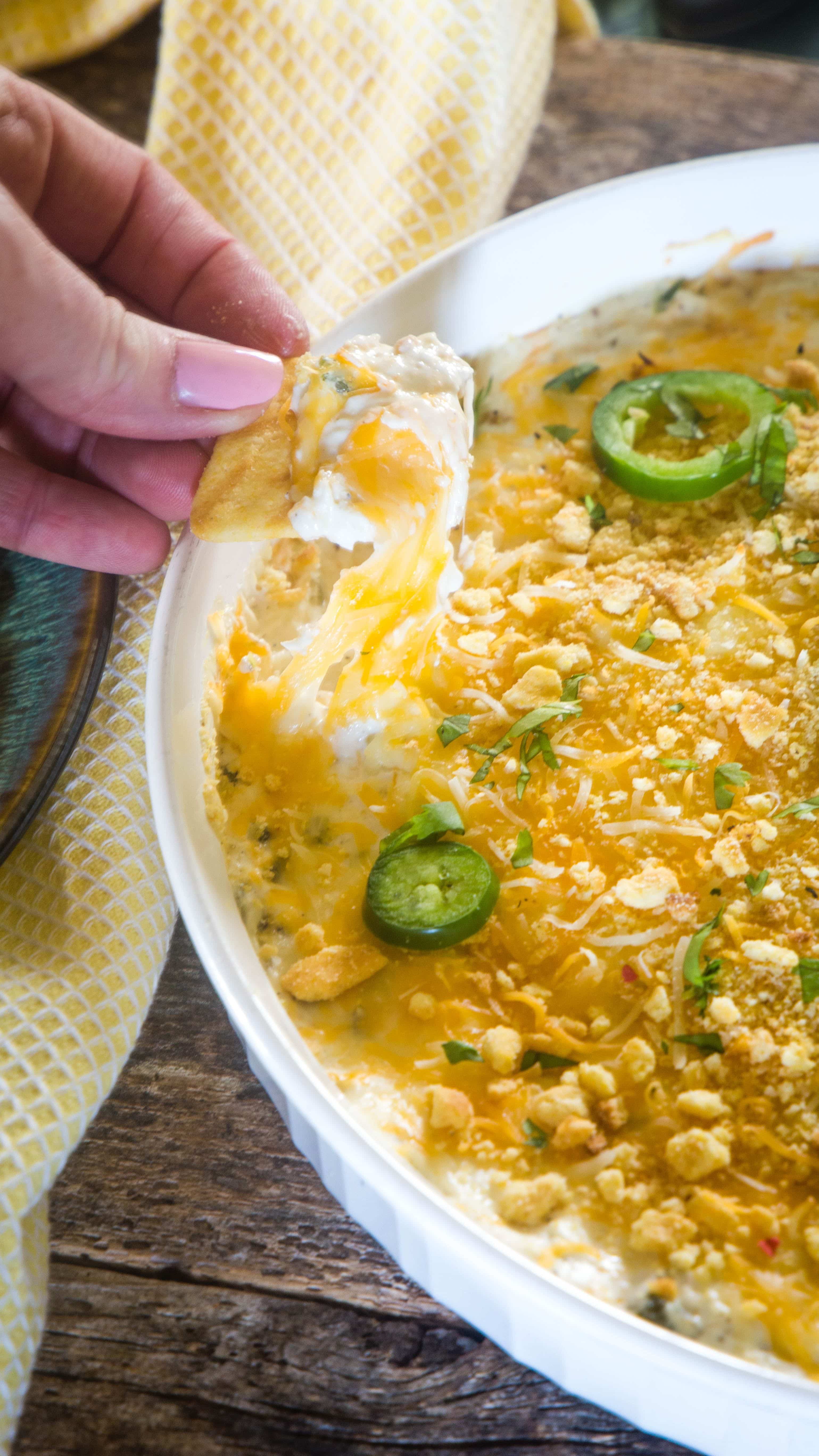 warm jalapeno popper dip topped with cheese and jalapeno with a cracker dipped into the dip