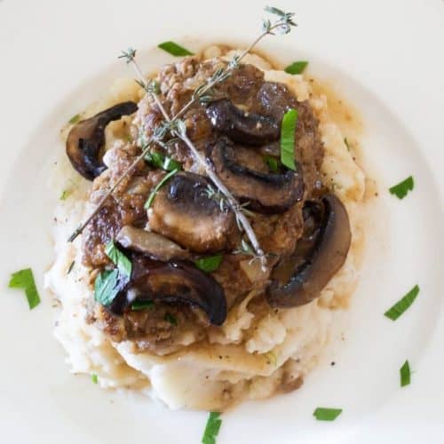 hamburger steaks topped with mushrooms and brown gravy on mashed potatoes