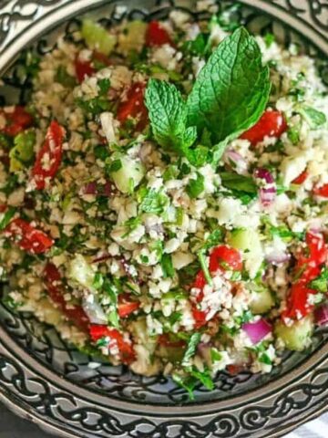 a delicious bowl of cauliflower tabbouleh with a vinaigrette and mint leaf in a silver bowl