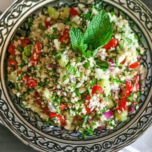 a delicious bowl of cauliflower tabbouleh with a vinaigrette and mint leaf in a silver bowl