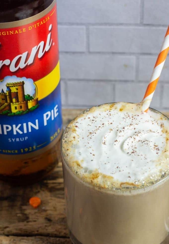 Pumpkin spice latte in a clear glass mug with Torani pumpkin spice syrup to the side