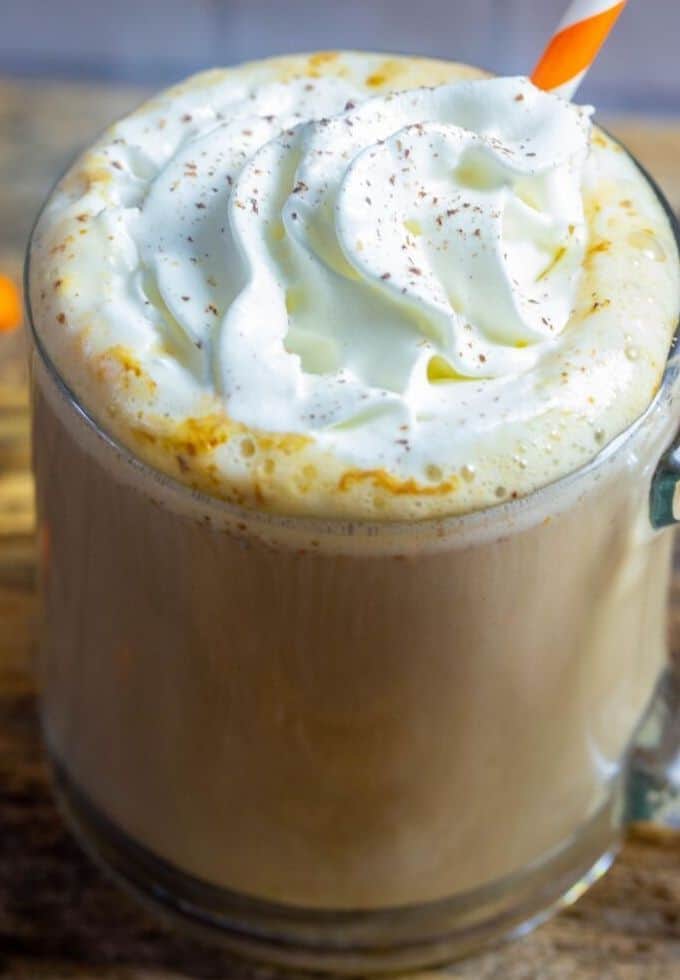 a pumpkin spice latte topped with cream in a clear coffee mug