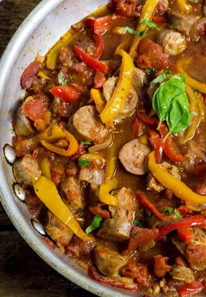 Saute pan filled with sausage and peppers topped with basil