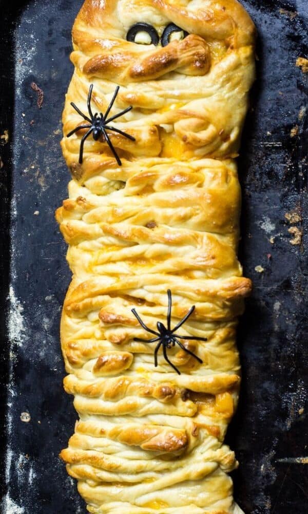 Festive taco meat mummy bread with fake spiders on the dough.