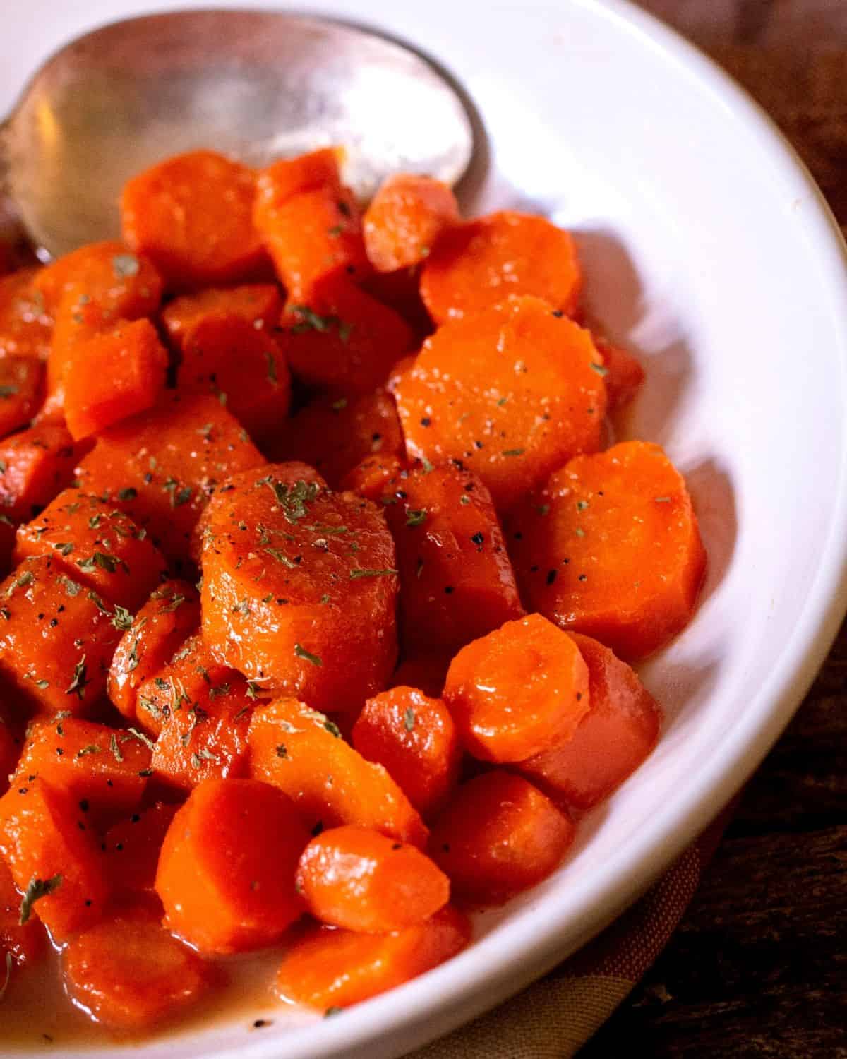 sliced carrots with a brown sugar and butter glaze in a bowl sprinkled with fresh parsley and black pepper