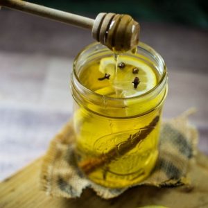 Delicious hot toddy in a mason jar with a honey stick over the jar dripping honey into the glass.