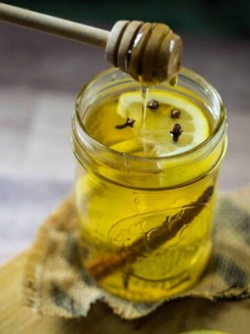 Delicious hot toddy in a mason jar with a honey stick over the jar dripping honey into the glass.