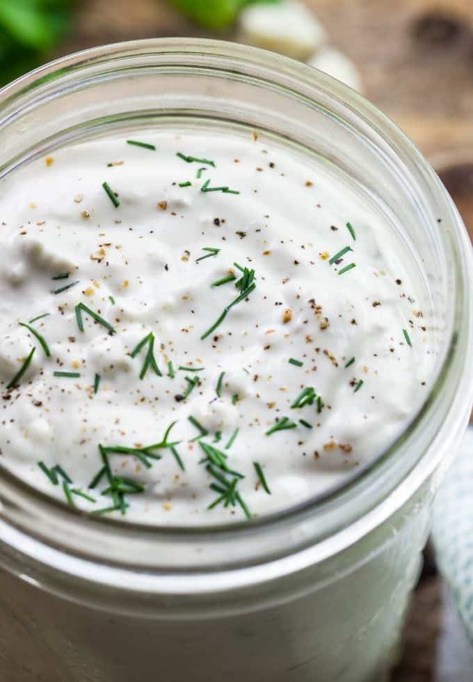 blue cheese salad dressing in a glass jar with cracked pepper and herbs garnishing the bowl