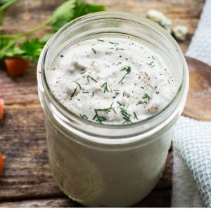 A mason jar filled with blue cheese dressing topped with fresh dill in a wooden table.