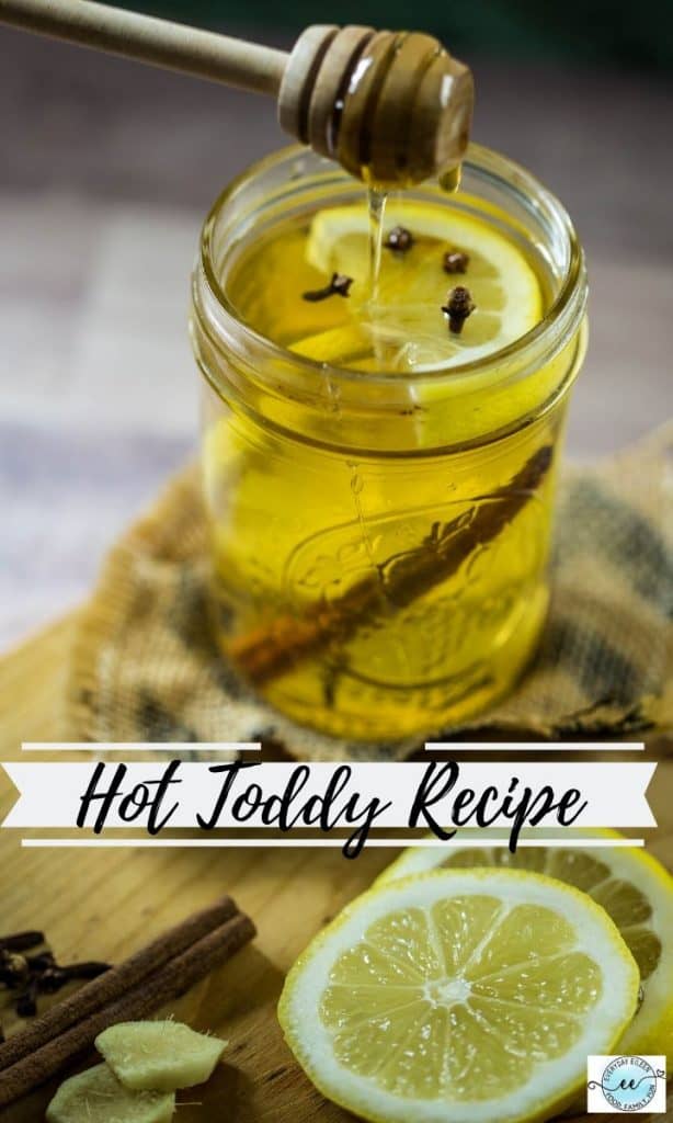 A glass mason jar filled with a light yellow liquid with a honey stick above the jar.