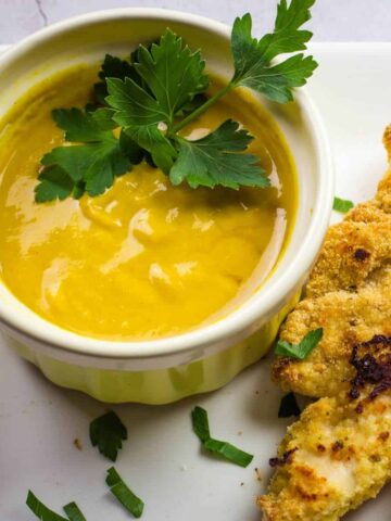 homemade honey mustard sauce with fresh parsley in a yellow bowl.