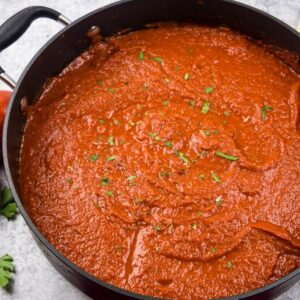 a large grey saucepan filled with tomato sauce topped with chopped parsley