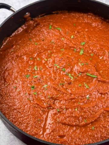 a large grey saucepan filled with tomato sauce topped with chopped parsley