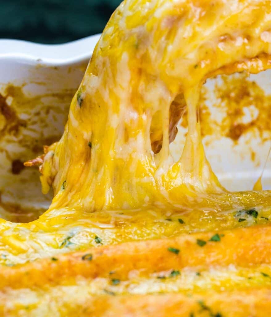 A cheesy rolled enchilada being lifted out of a casserole
